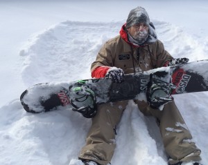 A man sitting in the snow holding his snowboard.