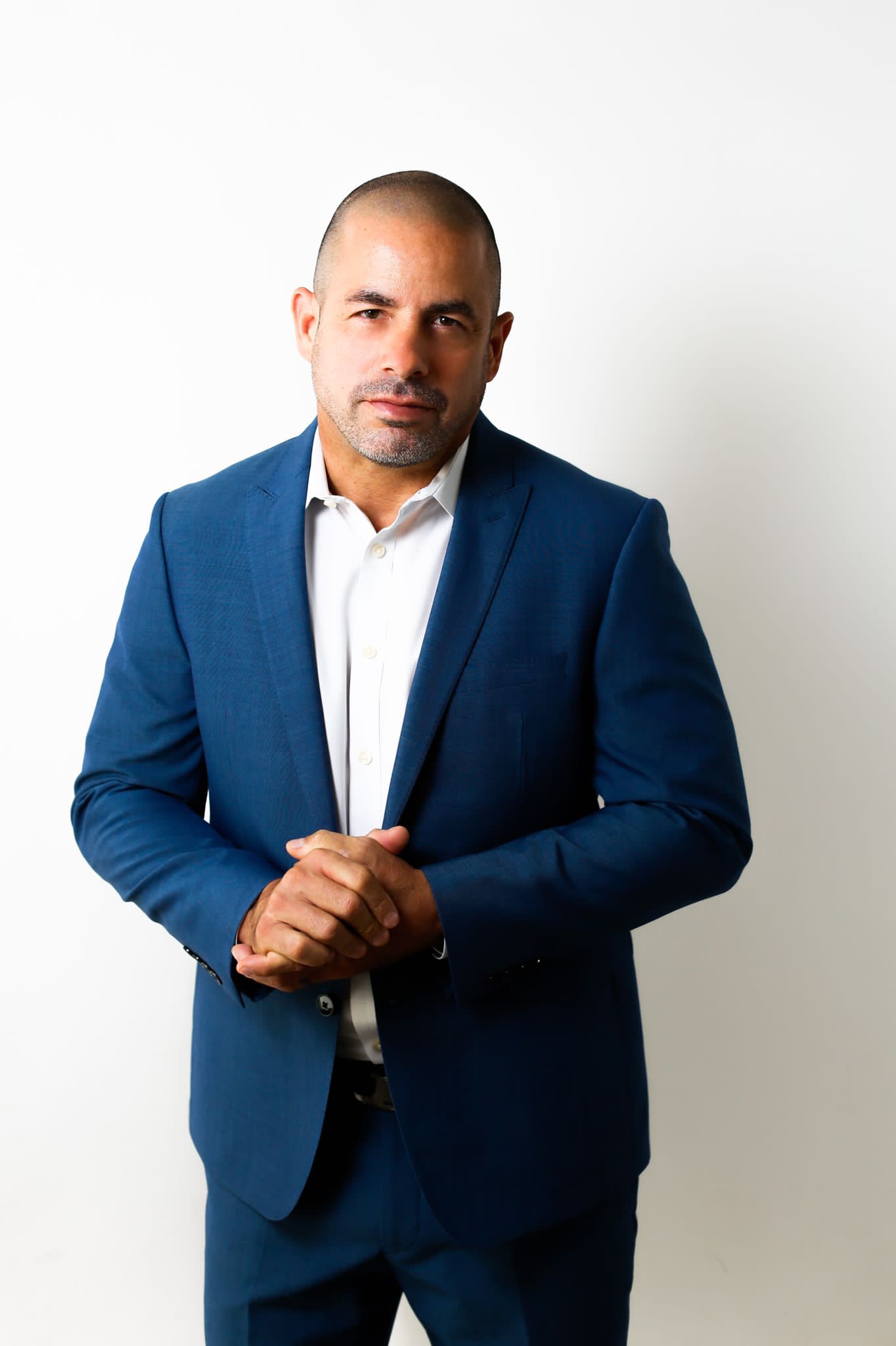 A man in a blue suit standing next to a white wall.